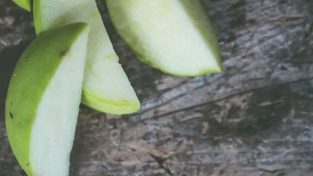 A gray-muzzled dog sniffing apple slices set on a kitchen floor