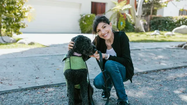 A woman crouches to greet a hesitant dog on a leash during an outdoor session