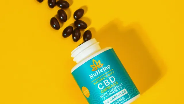An owner's hand holding a bottle of turmeric capsules beside a dog's food bowl