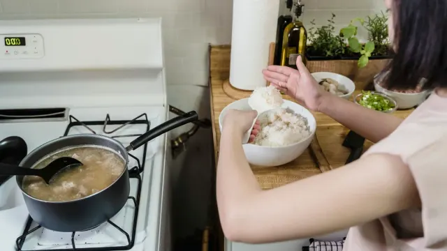 An owner spooning a supplement powder over a bowl of dog food on a kitchen counter