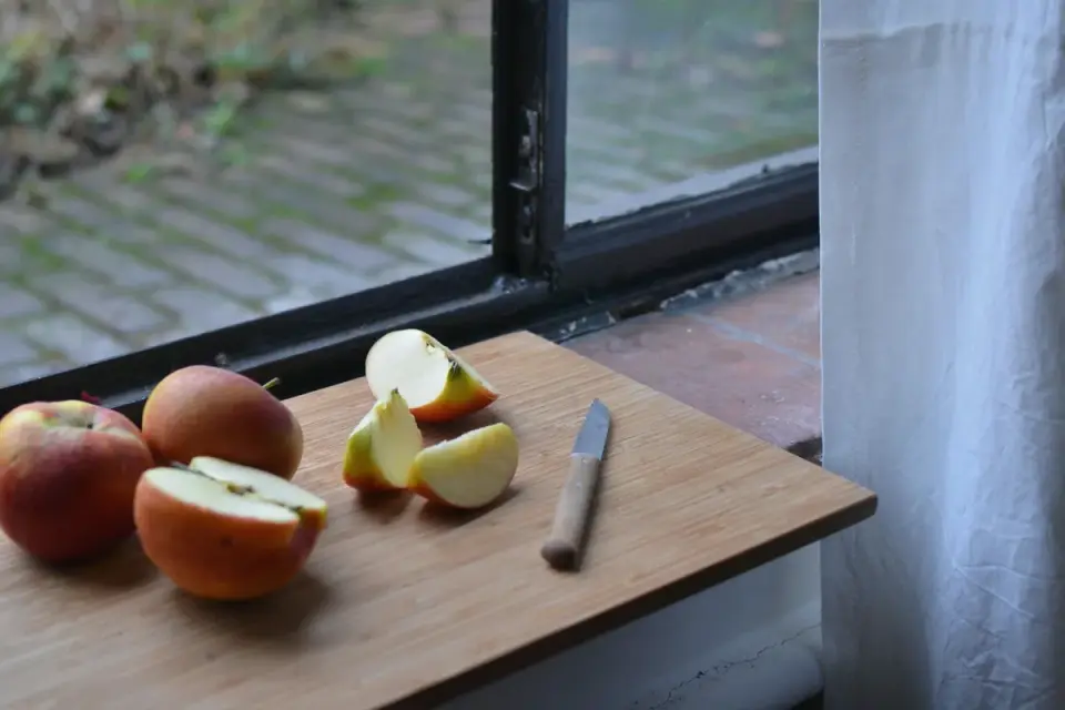 Cored apple slices on a wooden cutting board with a dog waiting nearby