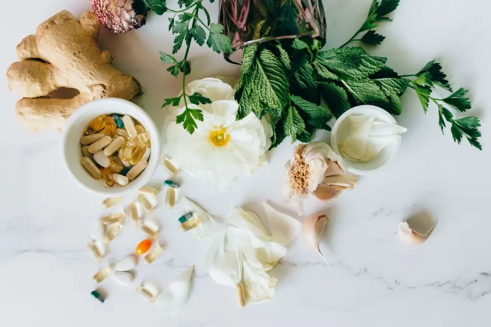Fresh ginger root next to dried chamomile flowers on a wooden surface